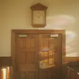Vintage wooden church clock frozen on the wall above sanctuary doors with stained glass light