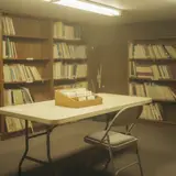 Dusty church library room with wooden shelves, aging paperbacks, and handwritten checkout cards on a folding table
