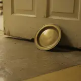 A brass offering plate used as a doorstop on a worn church fellowship hall floor