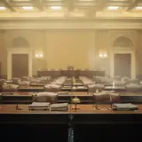 Empty congressional hearing room with rows of wooden desks and leather chairs under warm institutional lighting