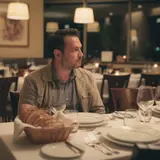 Man sitting alone at a large restaurant table surrounded by empty chairs and a bread basket